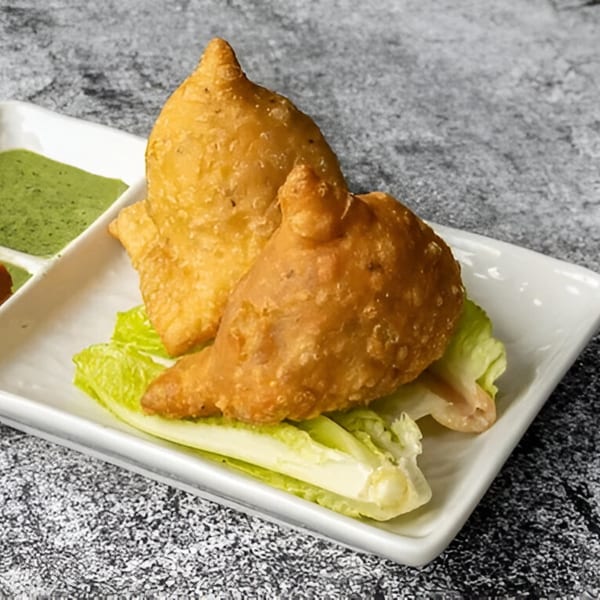 Two golden-brown Nepali samosas on a white plate with lettuce and green chutney.