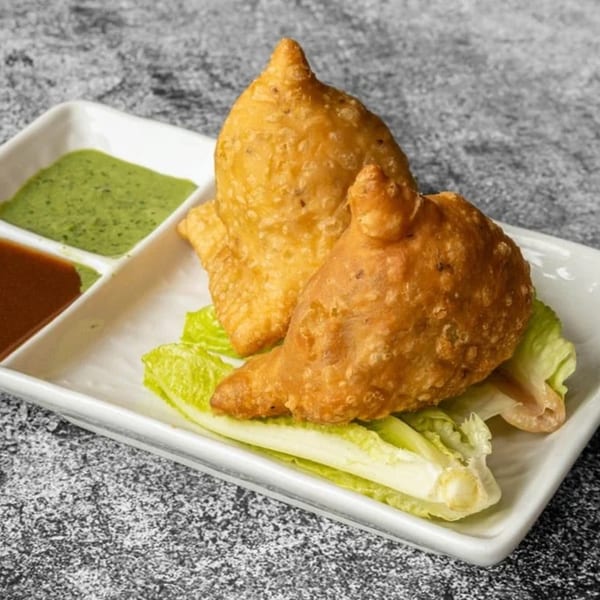 Two golden-brown Nepali samosas on lettuce, served with green and brown dipping sauces.