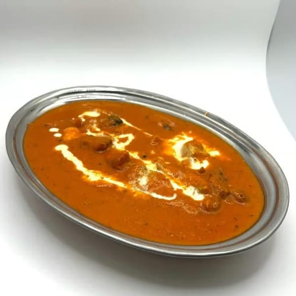 A metal oval dish filled with orange Nepali curry, garnished with white cream swirls.