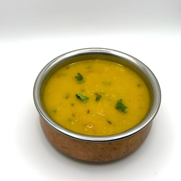 A copper bowl with a silver rim holds yellow Nepali dal, garnished with fresh green herbs.