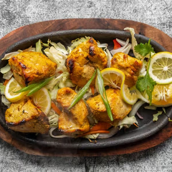 Sizzling Nepali chicken tikka with lemon slices, green onions, and cabbage on a dark plate.