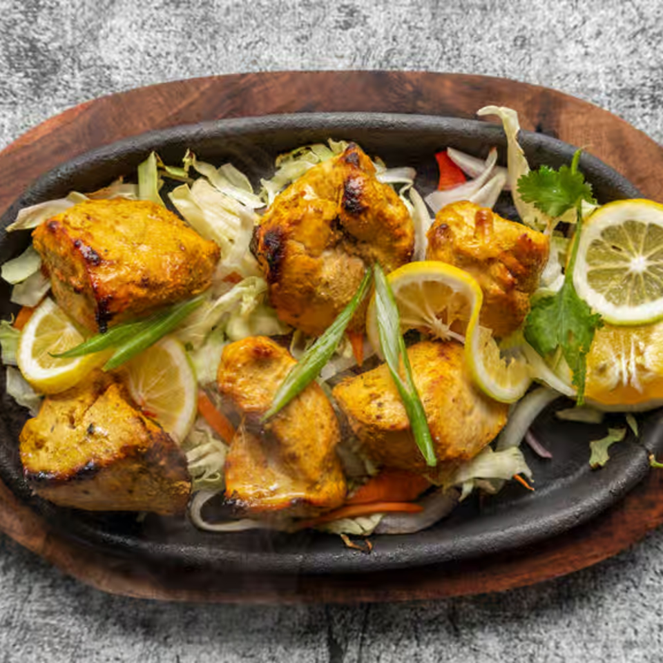 Sizzling Nepali chicken tikka with lemon slices, green onions, and cabbage on a dark plate.