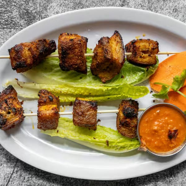 Two skewers of grilled Nepali pork belly, served with lettuce, carrot, and dipping sauce.