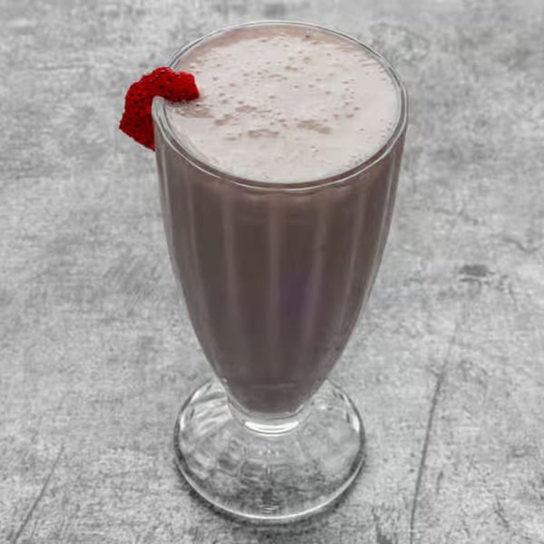 A glass of strawberry lassi, a traditional Nepali drink, garnished with a fresh strawberry slice.