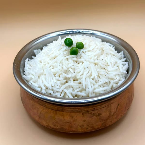 White basmati rice topped with three green peas, served in a copper bowl with a silver rim.
