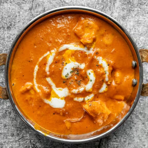 A metal bowl of orange Nepali curry with chicken, drizzled with white cream and spices.